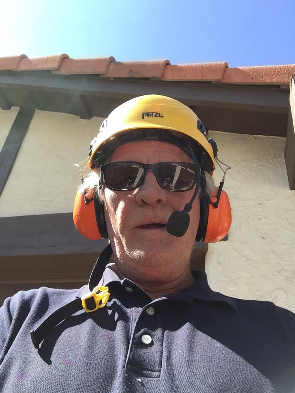 Man wearing a yellow Petzl hard hat, sunglasses, and orange earmuffs with a microphone.